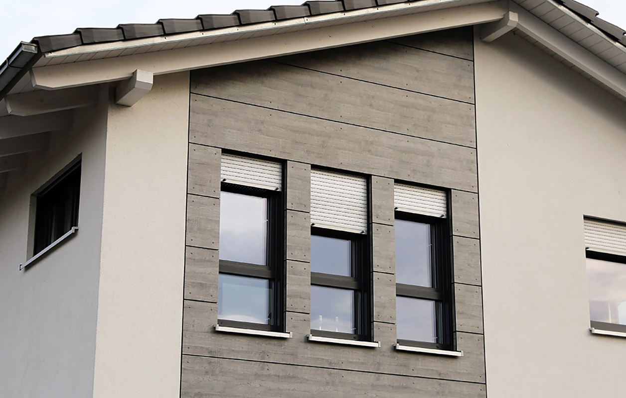 Hausfassade mit grauer Fassadenverkleidung rund um drei Fenster