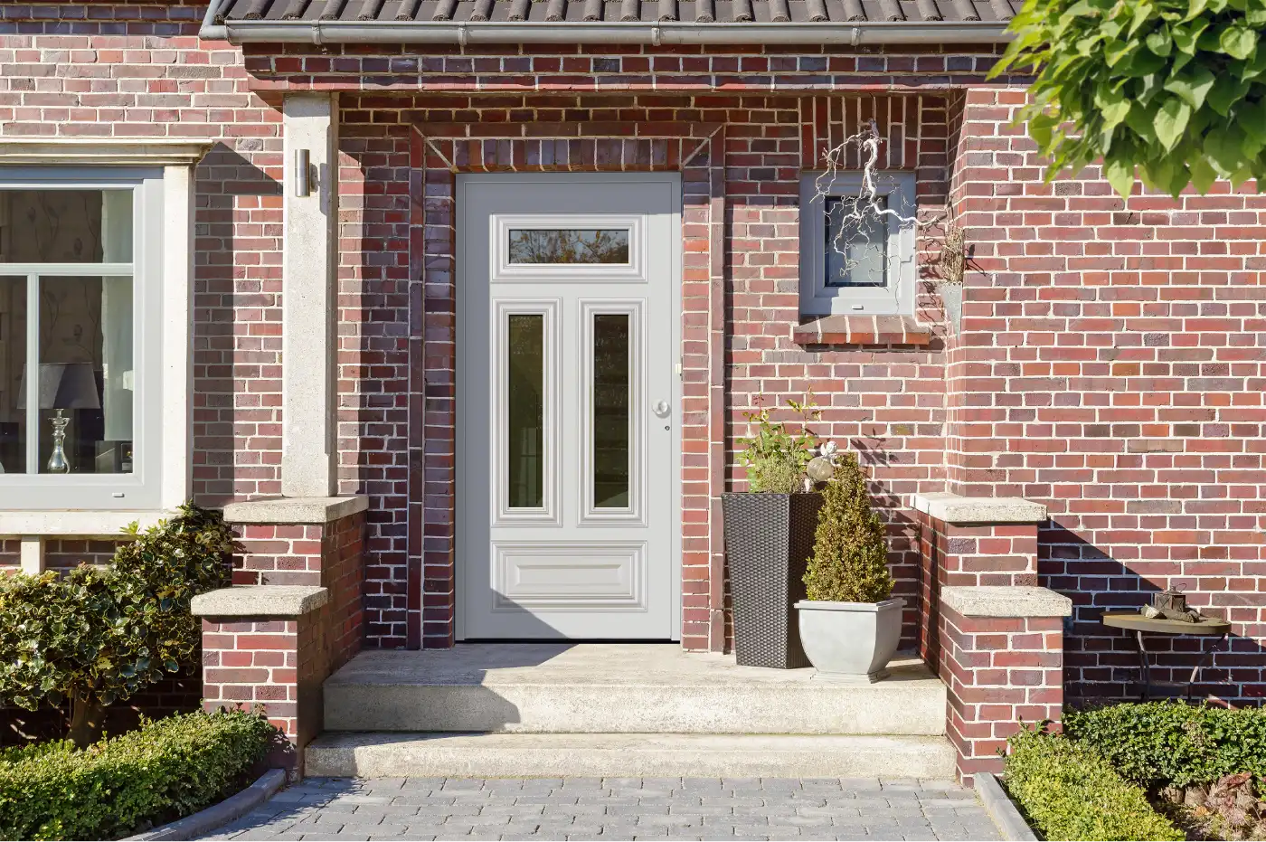 Klassische hellgraue Haustür mit mehreren Glasausschnitten an einem roten Klinkerhaus